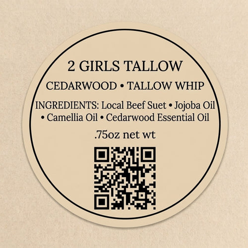 Round tan label reading "2 Girls Tallow, Cedarwood, Tallow Whip." Ingredients: local beef suet, jojoba oil, camellia oil, cedarwood essential oil. .75oz net wt. A QR code sits at the bottom.
